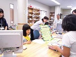 図書館大使が貸出をします。利用者の方もにっこり。（なんよう図書館　「子ども図書館大使」）